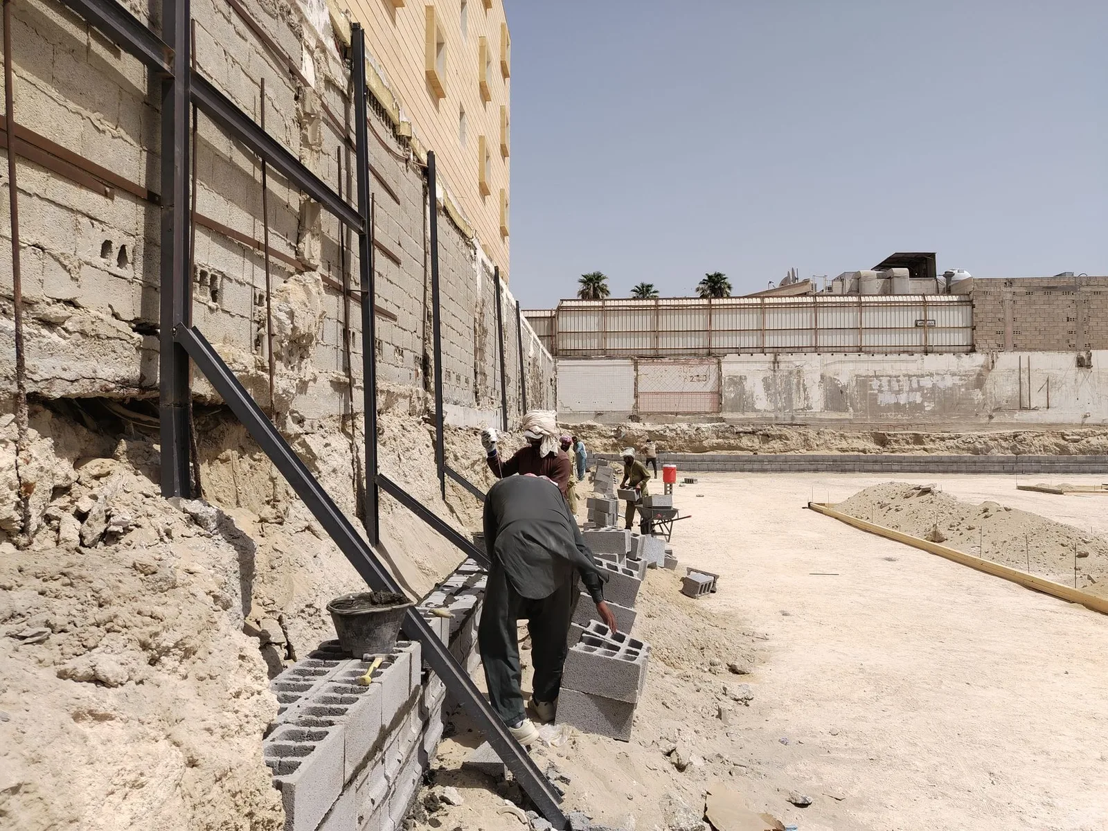 Workers building a concrete block retaining wall at a construction site under the clear sky.
